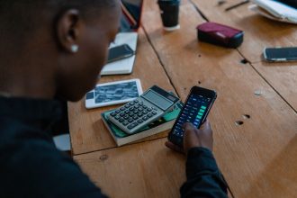 Pessoa analisa dados financeiros no celular, com uma calculadora sobre a mesa.
