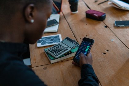 Pessoa analisa dados financeiros no celular, com uma calculadora sobre a mesa.